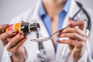 Hands of young woman doctor pouring medicinal syrup on spoon photo