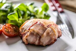 Meat wrapped in slices of bacon, baked until golden crispy and served with cherry tomatoes and green leave salad photo