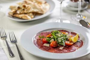 típico italiano aperitivo, carpaccio desde ternera o carne de vaca finamente rebanado y servido en un plato con ensalada foto