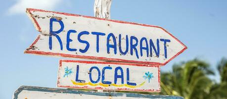 un firmar diciendo local restaurante puntos a el Derecha en un tropical verano destino, escrito en un rústico de madera blanco tablero foto