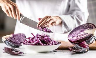 Chef takes remaining bits of cut red cabbage from a knife into a bowl photo