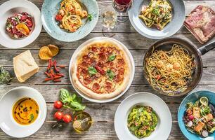 parte superior de ver lleno mesa de italiano comidas en platos y cacerola. Pizza pasta risotto sopa y pescado vegetal ensalada foto