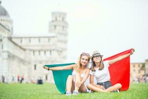 joven adolescente muchachas viajero con italiano bandera antes de el histórico torre en pueblo Pisa - Italia foto