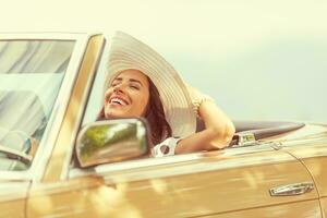 sonriente mujer disfrutando su verano cabrio paseo participación su sombrero con uno mano foto