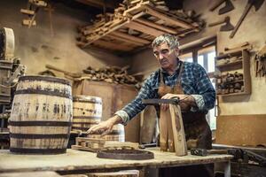 An aged craftsman builds wooden barrels in his vintage workshop photo