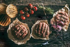 Raw burgers on wooden table with onion tomatoes herbs and spices photo