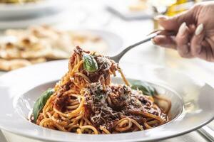 Female hand takes spaghetti pomodoro e basilico with parmesan cheese and basil on a fork photo