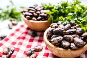 Uncooked beans in wooden bowles  with parsley herbs on kitchen table photo