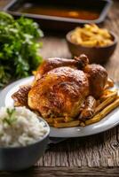 Roast chicken whole on a wooden cutting board with side dishes rice and french fries photo