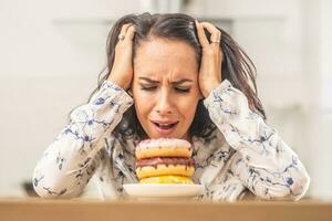 Woman holding her head by hands over irresistable pile of donuts photo