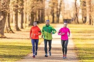 A trio of runners, two young women and one mature man are running in an autumn park photo