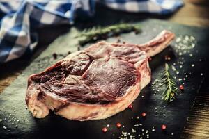 crudo carne de vaca tomahawk filete con sal pimienta y Romero en pizarra plato foto