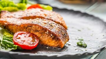 Delicious grilled roasted salmon fillets or steaks with sesame tomatoes and lettuce salad. photo