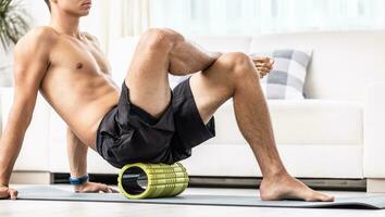 A young man massages the gluteal muscle with a foam roller photo