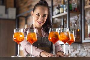 Barmaid offers aperol spritz cocktails on a bar smiling at the camera photo