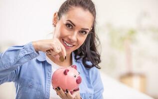 Saving money into a pink piggybank by a brunette woman holding a copper coin photo