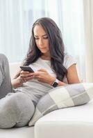 Attractive woman in sweatpants and t-shirt texting on a phone in a white light background of her apartment photo