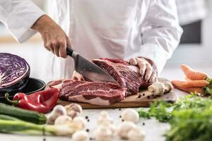 rebanar carne de vaca o Cerdo pedazo con cuchillo en un profesional restaurante cocina foto