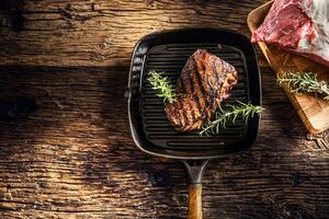 Grilled beef steak in grill pan with herbs rosemary on wooden table photo