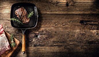 Grilled beef steak in grill pan with herbs rosemary on wooden table photo