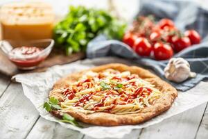 Tasty deep-fried langos served on baking paper with a lot of grated cheese, ketchup, fresh herbs and tomatoes on a checked dish cloth photo