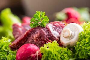 Raw beef meat with fresh vegetable. Sliced beef steak in lettuce salads radishes and mushrooms. photo