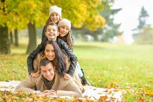 Family with children lying down on a blanket making a human pyramid in the nature on a fall day photo