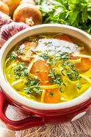 Chicken soup broth in a vintage bowl with homemade noodles carrot onion celery herbs garlic and fresh vegetables photo