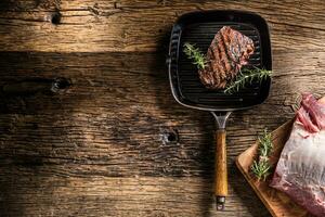 Grilled beef steak in grill pan with herbs rosemary on wooden table photo