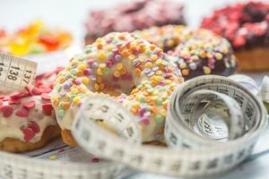 Sweet glazed donuts and measure tape on table photo