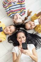 Mom and three kids lie on the floor, each of them holding a cell phone in hands photo