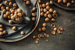 Top view of hazelnuts and their cracked shells on a rustic dark metallic background, in a metallic cup and on a tray photo