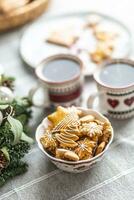 un cuenco lleno de Navidad pan de jengibre en el mesa LED un adviento guirnalda y dos tazas con café, puñetazo o té foto