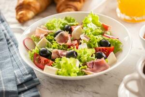 Healthy salad in a bowl with olives, raddishes, tomato, cheese and lean ham served for breakfast photo