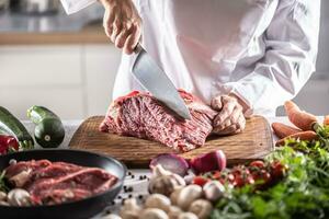 Chef cuts a slice from a chunk of red meat by a big knife in the restaurant photo