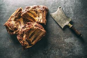 Top view of smoked ribs on a dark metallic surface next to a vintage knife photo