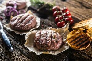 Raw burgers on wooden table with onion tomatoes herbs and spices photo