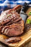 Freshly grilled tomahawk steak on slate plate with salt pepper rosemary and parsley herbs. Sliced pieces of juicy beef steak photo