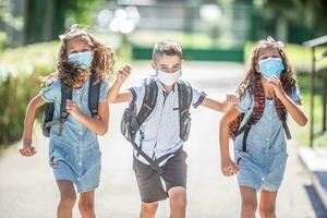 Happy schoolchildren with face masks run from the joy of returning to school during the Covid-19 quarantine photo