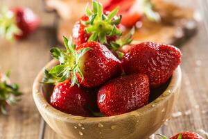 Juicy washed strawberries in wooden bowl on kitchen table photo