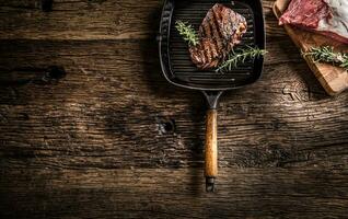 Grilled beef steak in grill pan with herbs rosemary on wooden table photo