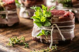 Raw steak wrapped with bacon and fresh herbs on a wooden cutting board. photo