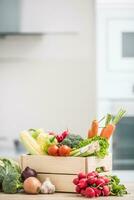 Wooden box full of fresh healthy vegetables. Broccoli carrot radish onion garlic corn on wooden kitchen table photo