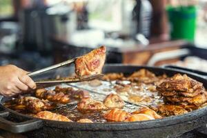 mano participación un pedazo de carne tomado desde un grande fritura pan en cocina alicates foto