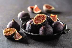 A few figs in a black bowl on an dark concrete table photo