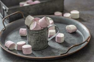 Metallic vintage tray, surface and cup with pink and white marshmallows inside the cup and scattered around the tray as well as in the metallic box in the background photo