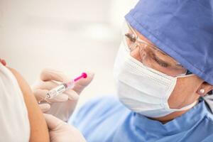 Detail of an injection of a SARS-CoV-2 vaccine being shot to a shoulder of a patient. photo