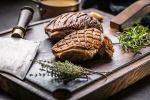 Crispy baked duck breast on a cutting board with rosemary and thyme herbs photo