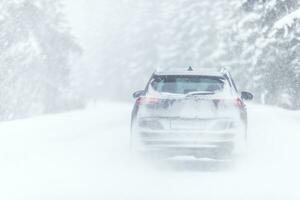 Car covered in snow driving in snowstorm on a cold winter day in the forest photo