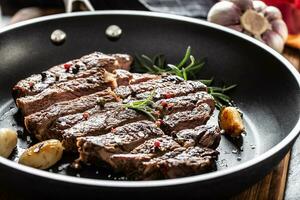 Juicy and grilled beef Rib Eye steak in teflon pan with salt, pepper and rosemary herbs photo